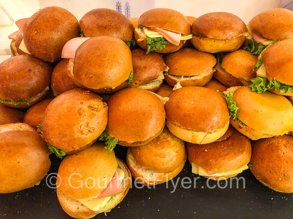 A pile of sandwiches made with deli meat and mini buns.