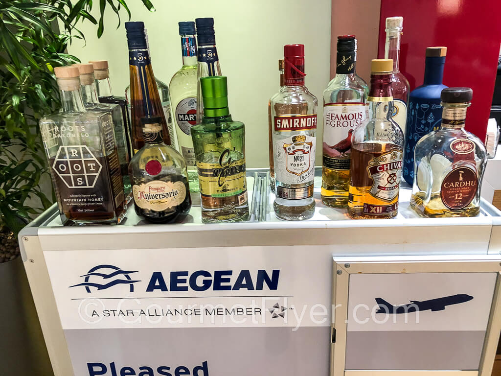 More than a dozen bottles of liquor sit on top of a beverage cart with the Aegean logo.