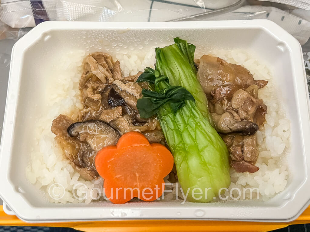 A close-up of the pork dish served with white rice and Chinese vegetables.