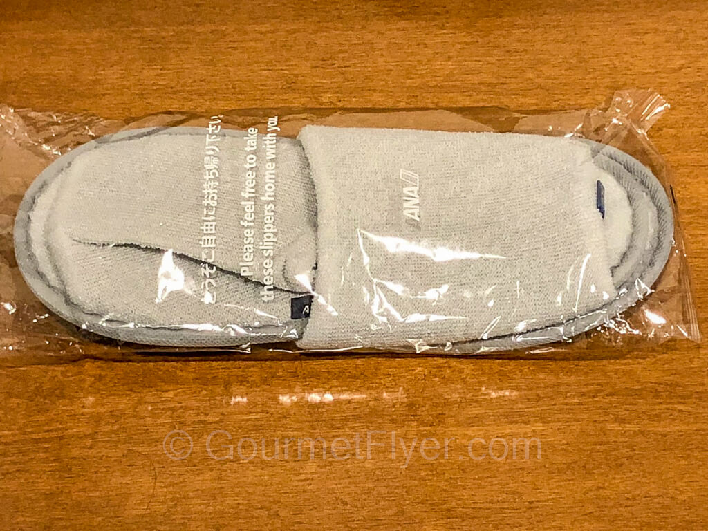 A pair of gray fabric slippers wrapped in a plastic bag.