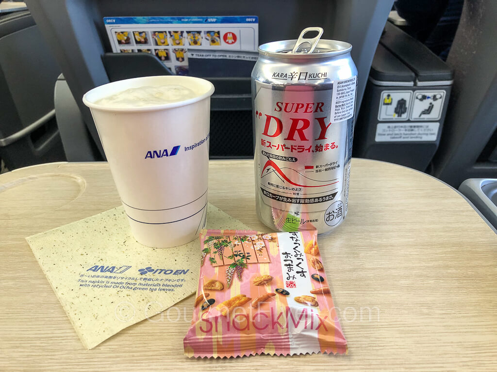 A can of Asahi Super Dry beer is served in a paper cup with a bag of Japanese snacks.