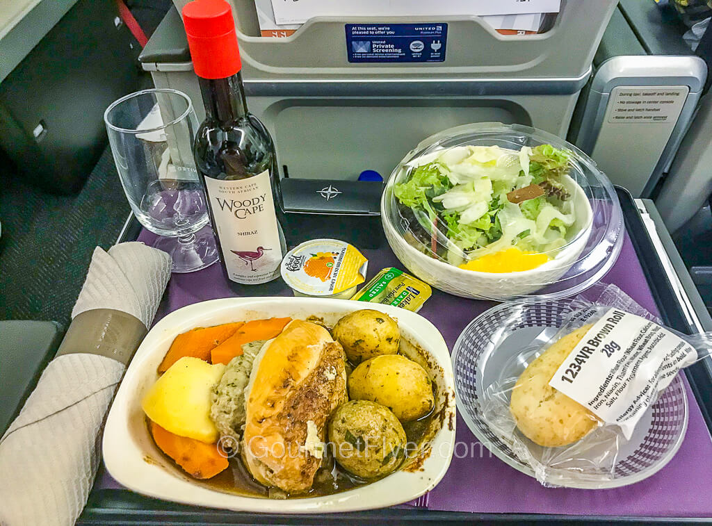 Review of United's Premium Plus Premium Economy features a dinner with chicken breast and vegetables and accompanied by a small bottle of red wine.