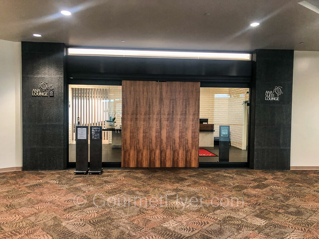 Entrance to the ANA Lounge with a pair of closed wooden doors on carpeted floor.