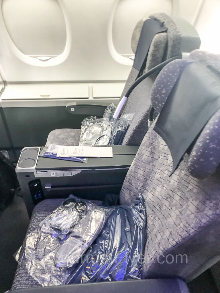 A pair of premium economy seats with purple fabrics on the window side with the shades closed.