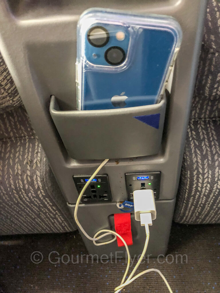 A blue iPhone is placed in the phone holder bracket while it is plugged into the power outlet.