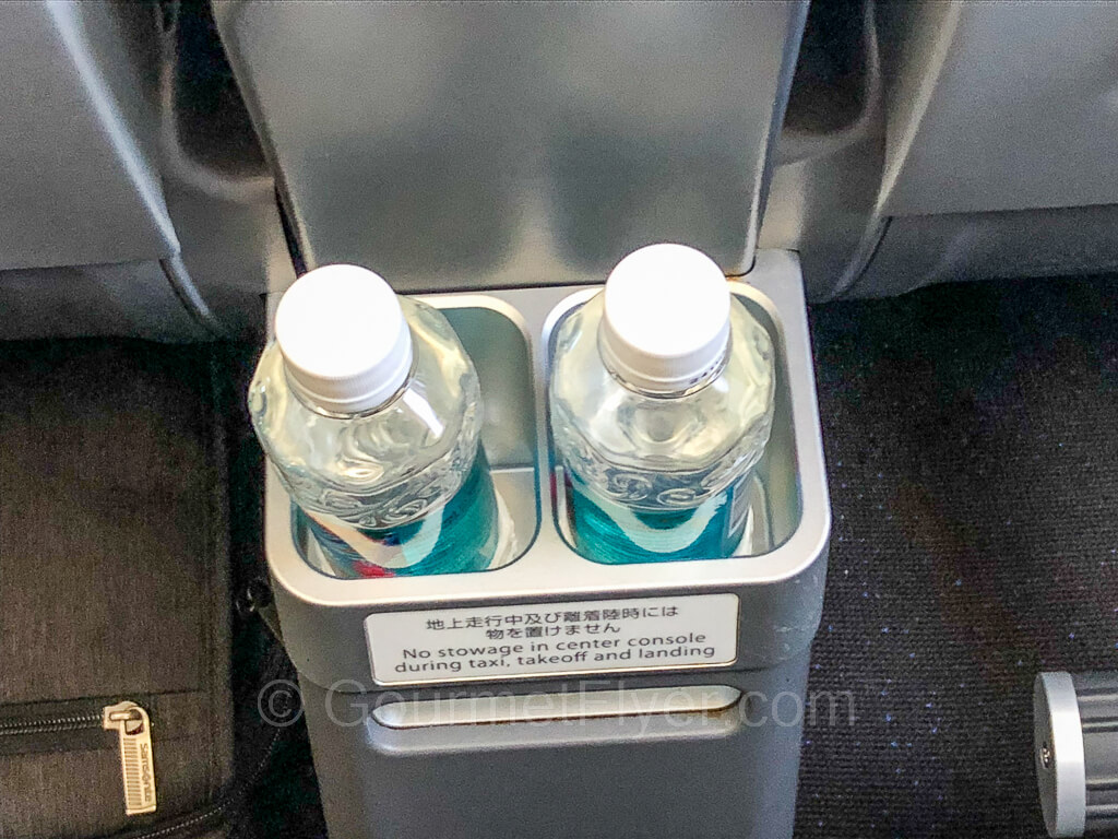 A pair of bottled waters are placed inside the holders in the center console of the seat in front.