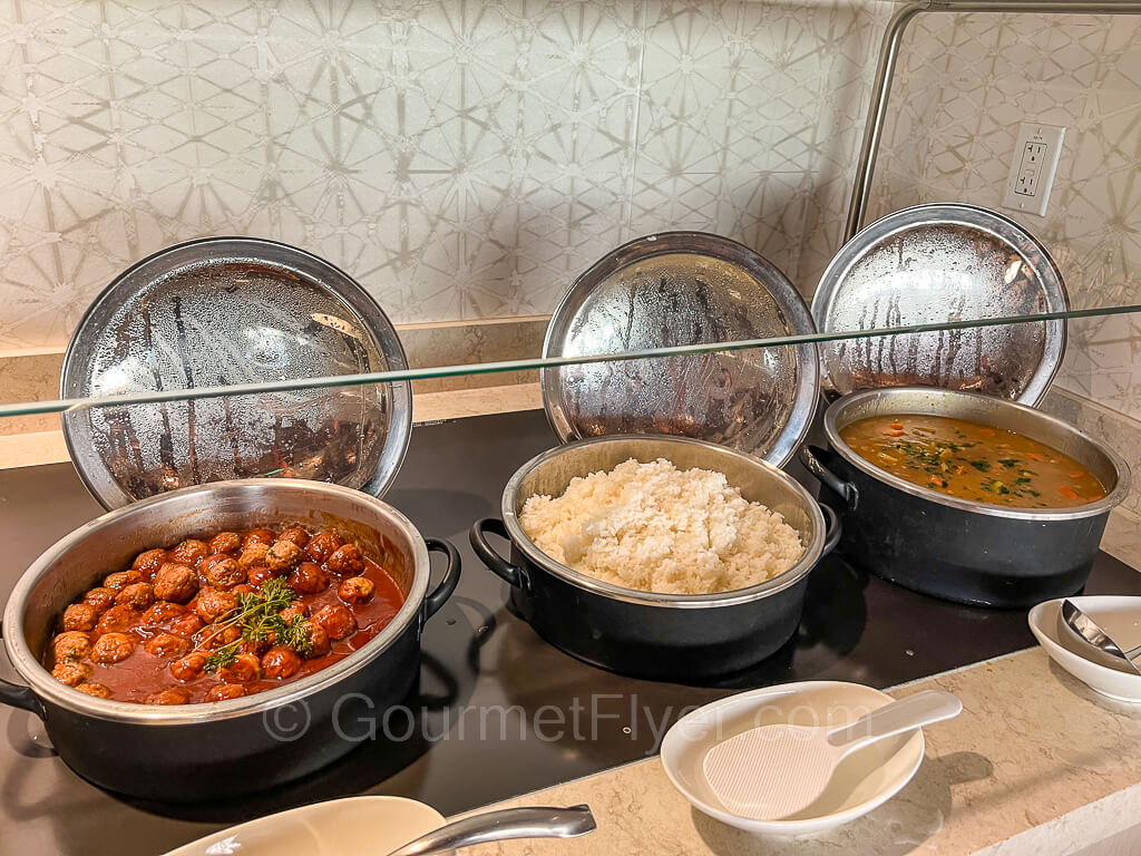 Serving pans of hot food on the counter, from left, meatballs in tomato sauce, white rice, and curry chicken.