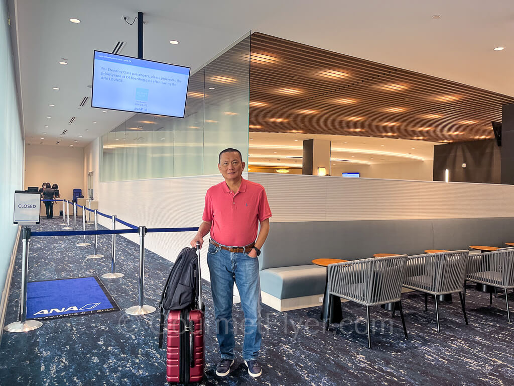 The Gourmet Flyer is standing in front of the boarding lanes at the lounge with his luggage.