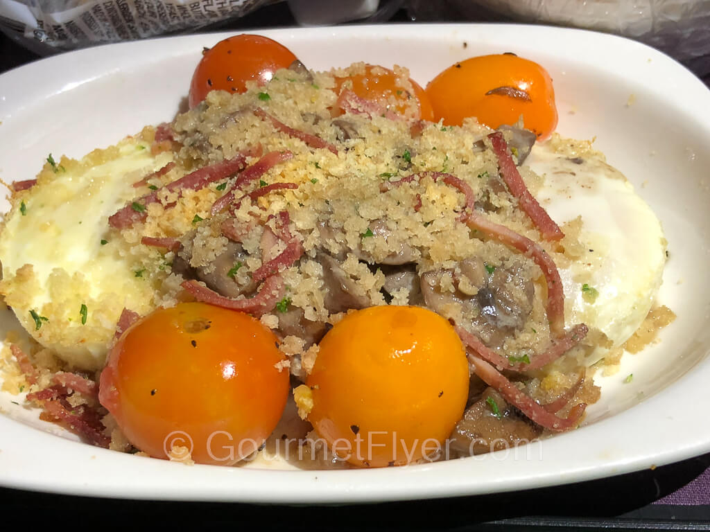 Two baked eggs are topped with cheese and onions and garnished with cherry tomatoes.