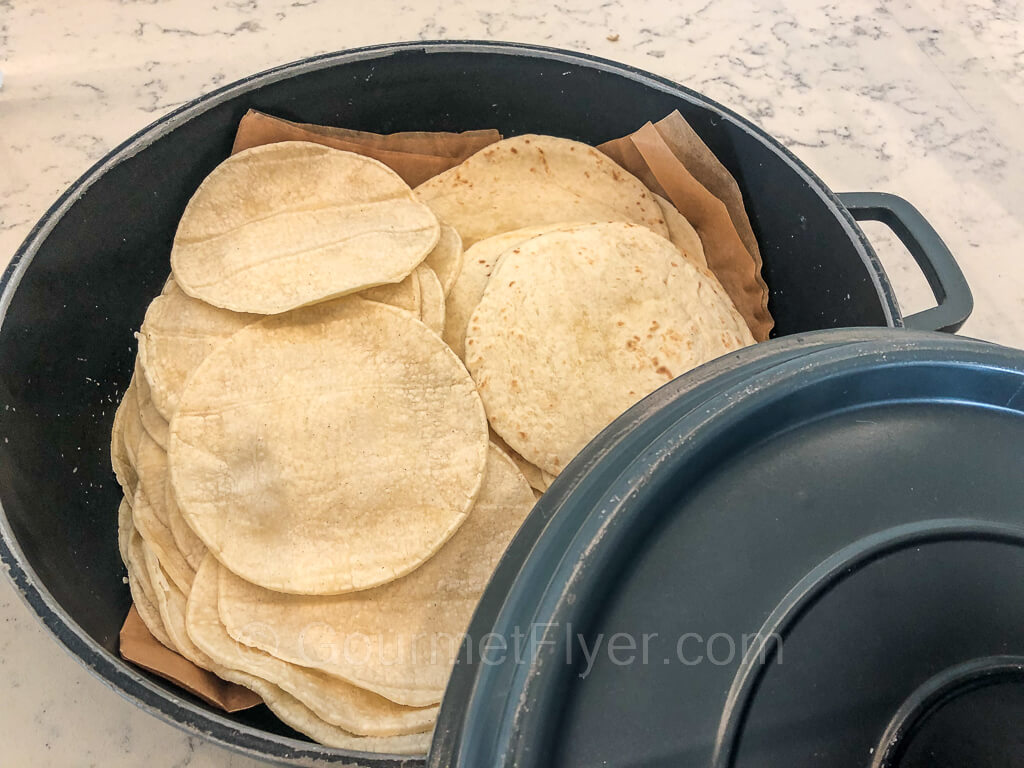 A pile of small flour tortillas is placed in a cast iron warmer.