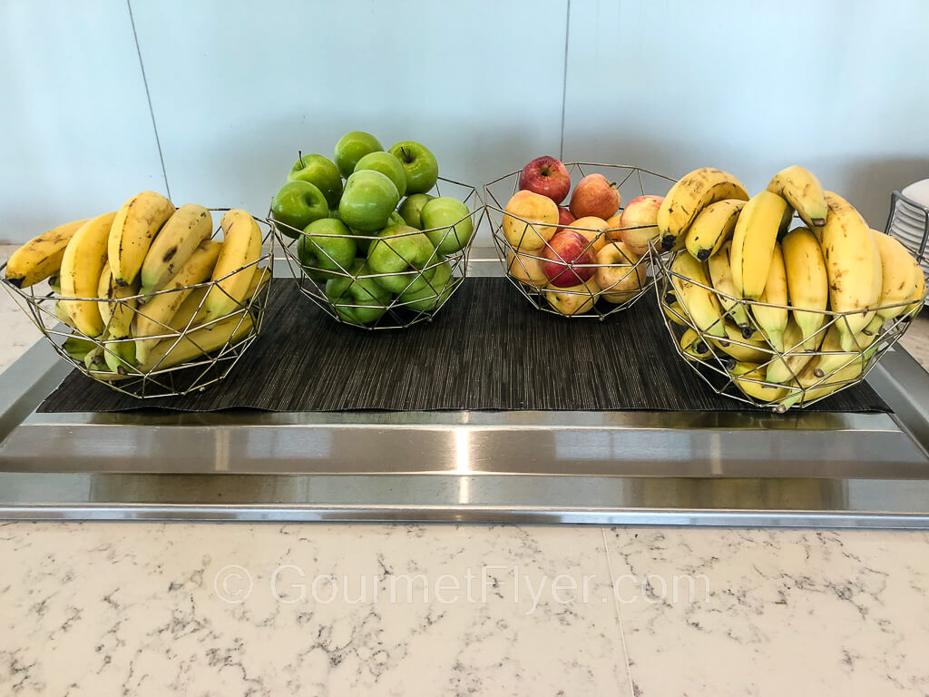 Bananas along with red and green apples are placed in bowls in a counter.