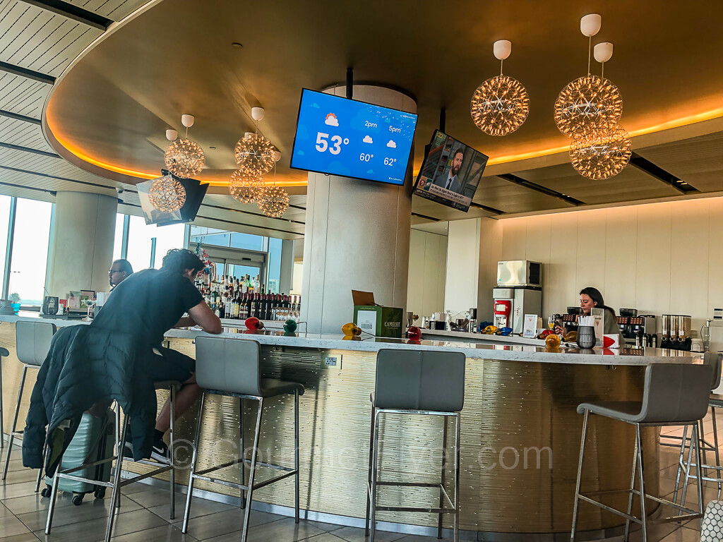 A circular shaped bar with bar stools. A bartender is there with two customers seated at the bar.
