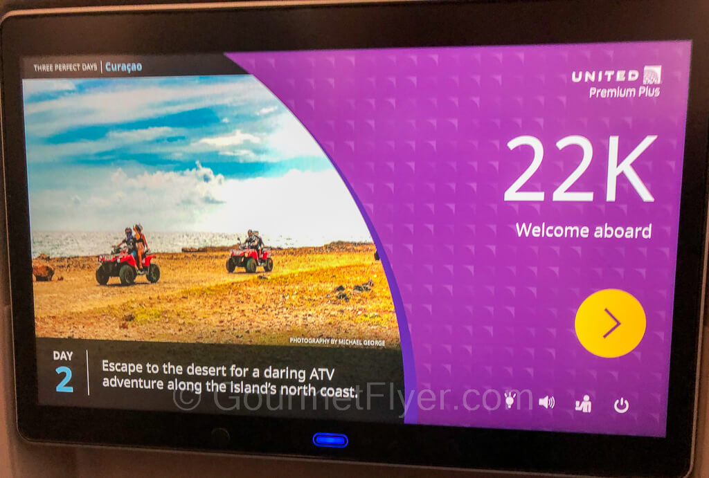 A close-up of the Premium Plus seatback with the seat number 22K shown on a purple screen, with ATVs in a desert in the background.