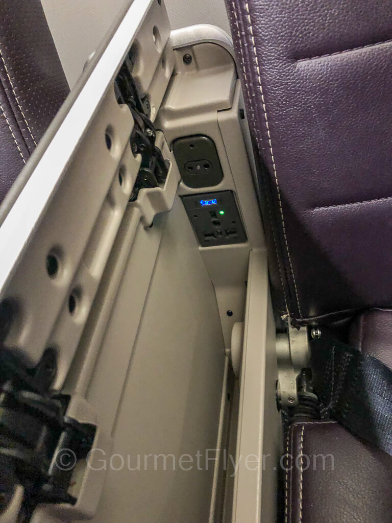 Armrest is flipped over to expose power outlet and headphone jacks, which are located next to the purple color seatback.