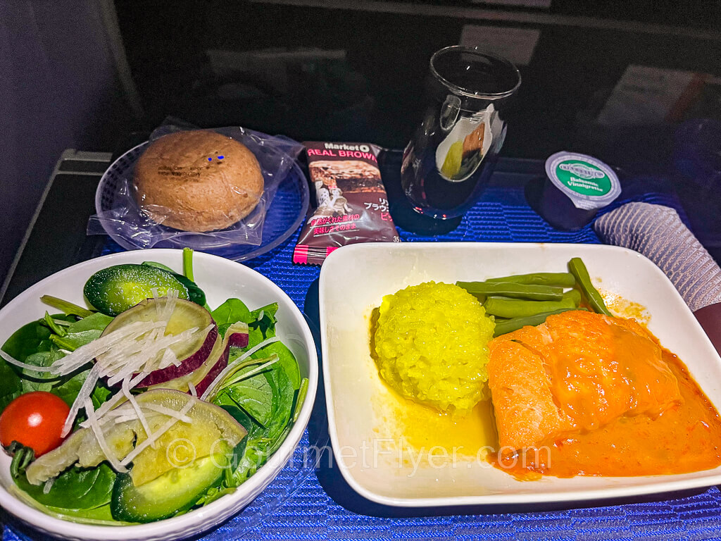 A dinner tray with the salmon main dish was served with risotto and accompanied by a salad, roll and butter, and a glass of red wine.