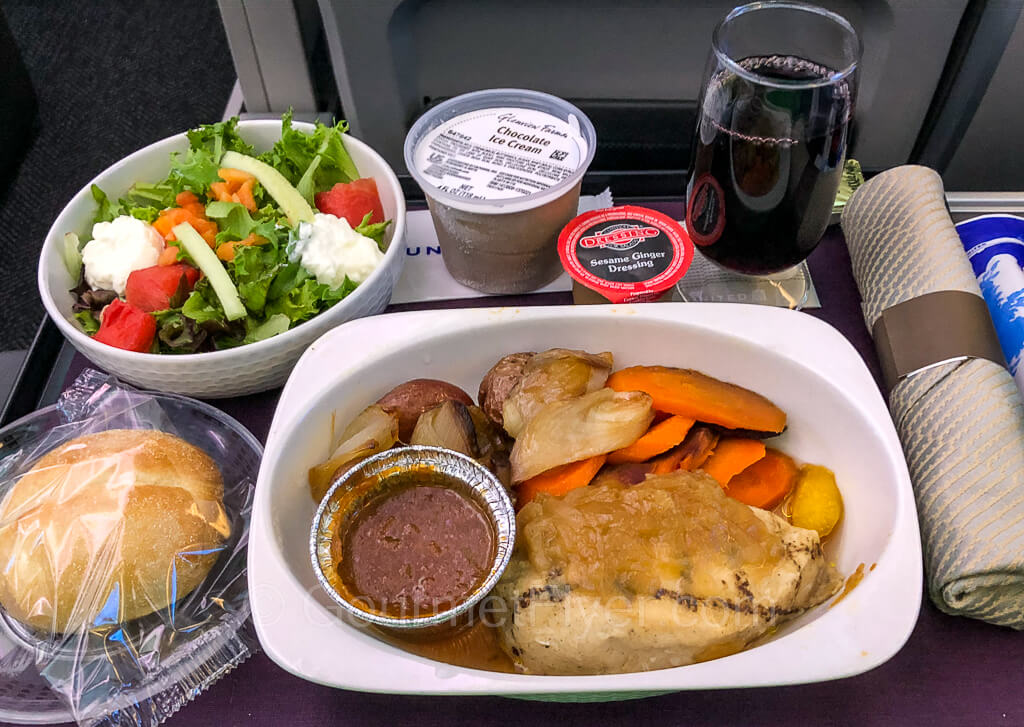 A tray of Premium Plus dinner service consisting of chicken, salad with dressing, bread, and dessert.