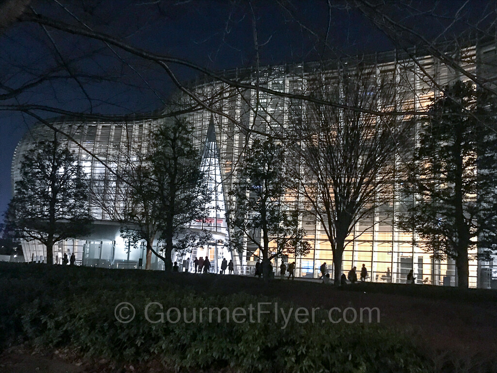 The night view of the National Art Center illuminated by a wall of windows lit from the inside.