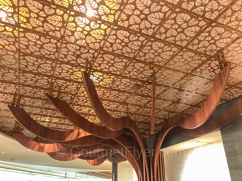 A banyan tree's wooden sculpture extends into the ceiling with tropical palm leaves images.