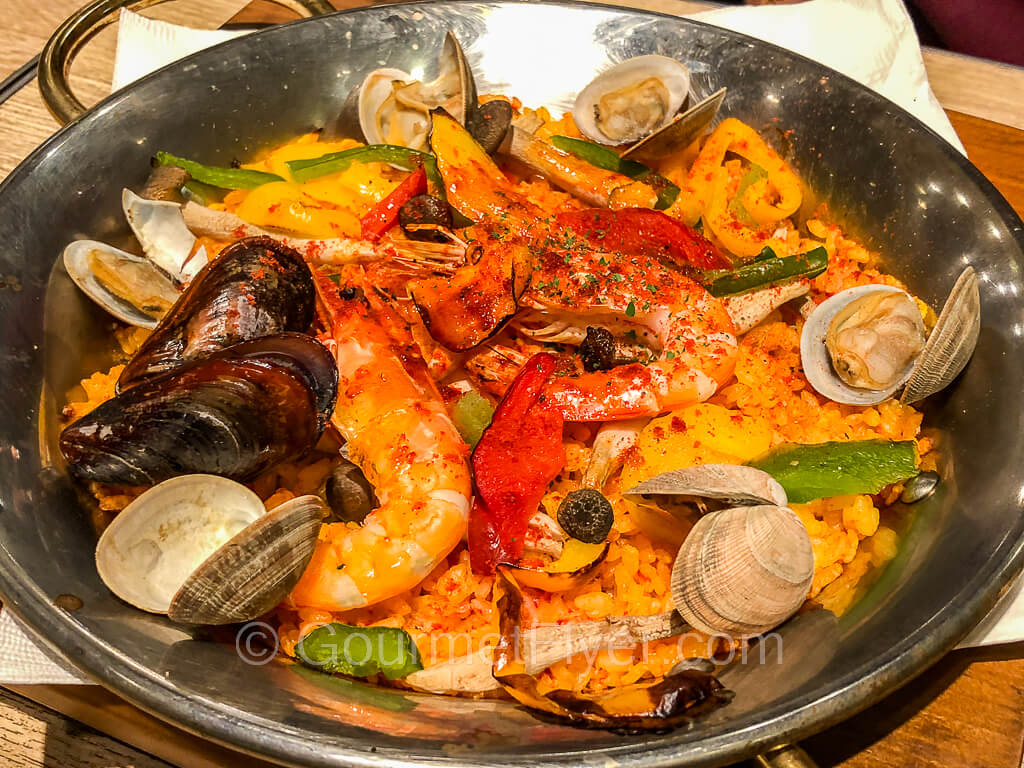 A paella dish with shrimps. clams, mussels, and fish, and garnished with onions and peppers.
