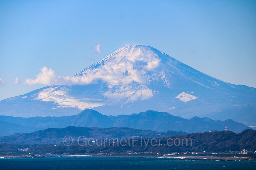 Mount Fuji on a clear day, with few white clouds neat the top and only little snow on its summit.
