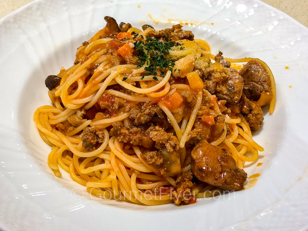 A plate of spaghetti Bolognese with chunks of beef and garnished with a sprinkle of parsley.