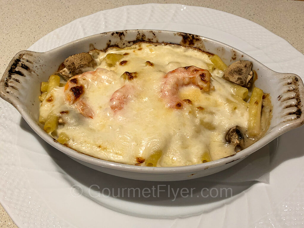 A baking dish with baked pasta covered with cheese and a few shrimps.
