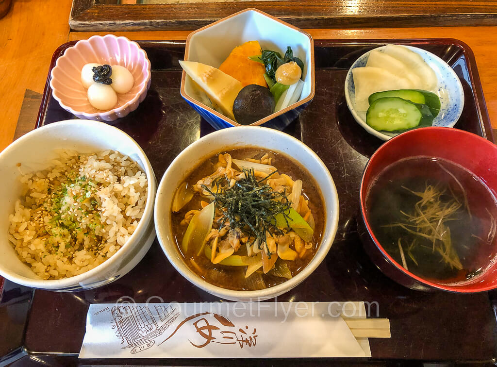 A dinner tray with two types of clam rice. a bowl of soup, and small plates of vegetables and mochi.