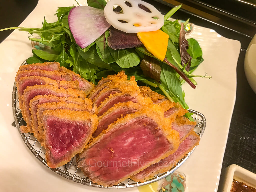 Sliced gyukatsu which is beef fried on the outside but rare on the inside is served on a plate accompanied by a green salad.