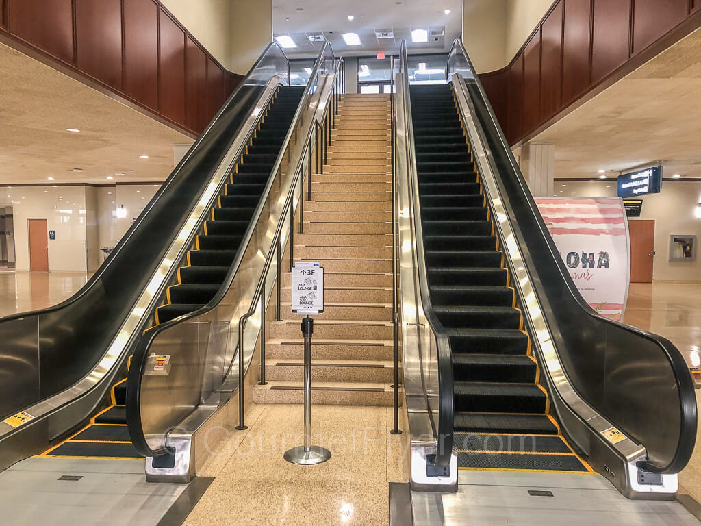Two long escalators are separated by a set of stairs. An ANA Lounge sign is at the bottom of the staircase.