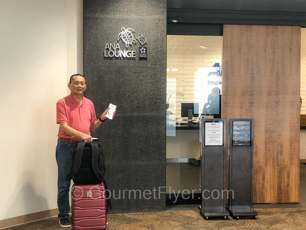 The Gourmet Flyer at the entrance of the ANA lounge with his luggage in one hand and his boarding pass in the other.