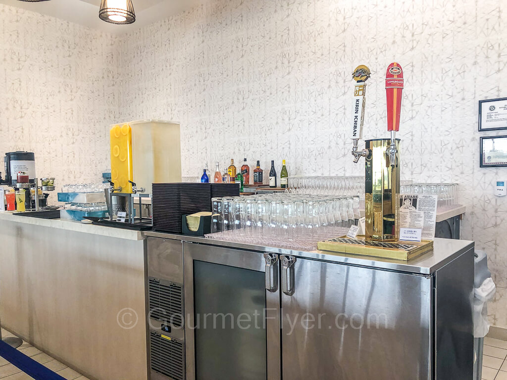 Two beers on tap are accompanied by dozens of glasses. A water and soft drink station is located to the left of the beer dispensers.