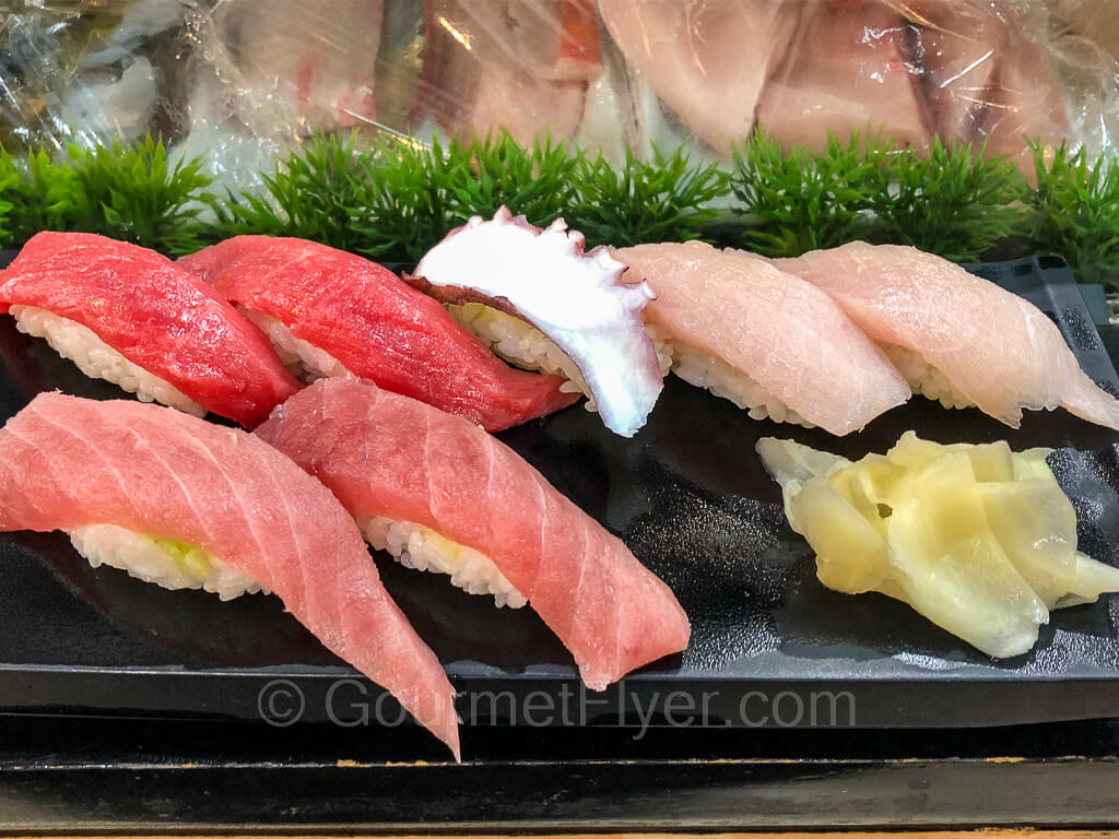 A plate of sushi is served at a sushi bar. The platter consists of red tuna, fatty tuna, octopus, and yellow tail.