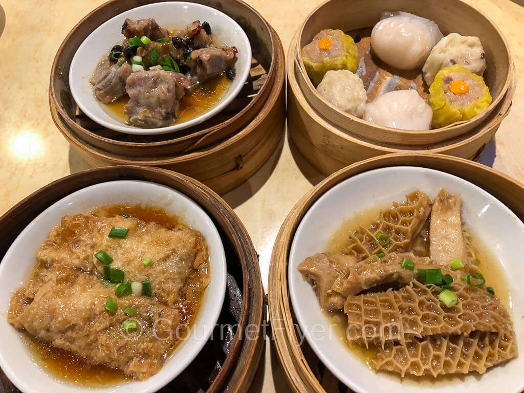 Four steam baskets of dim sum sit on a table. From upper left clockwise, pork spareribs, dumplings, beef tripes, and bean curd rolls.