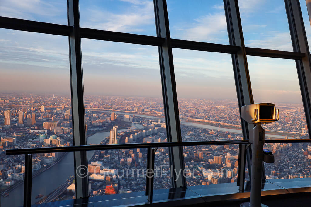 Large glass windows of the Tembo Galleria overlooking Tokyo and the river. A telescope is available for use.