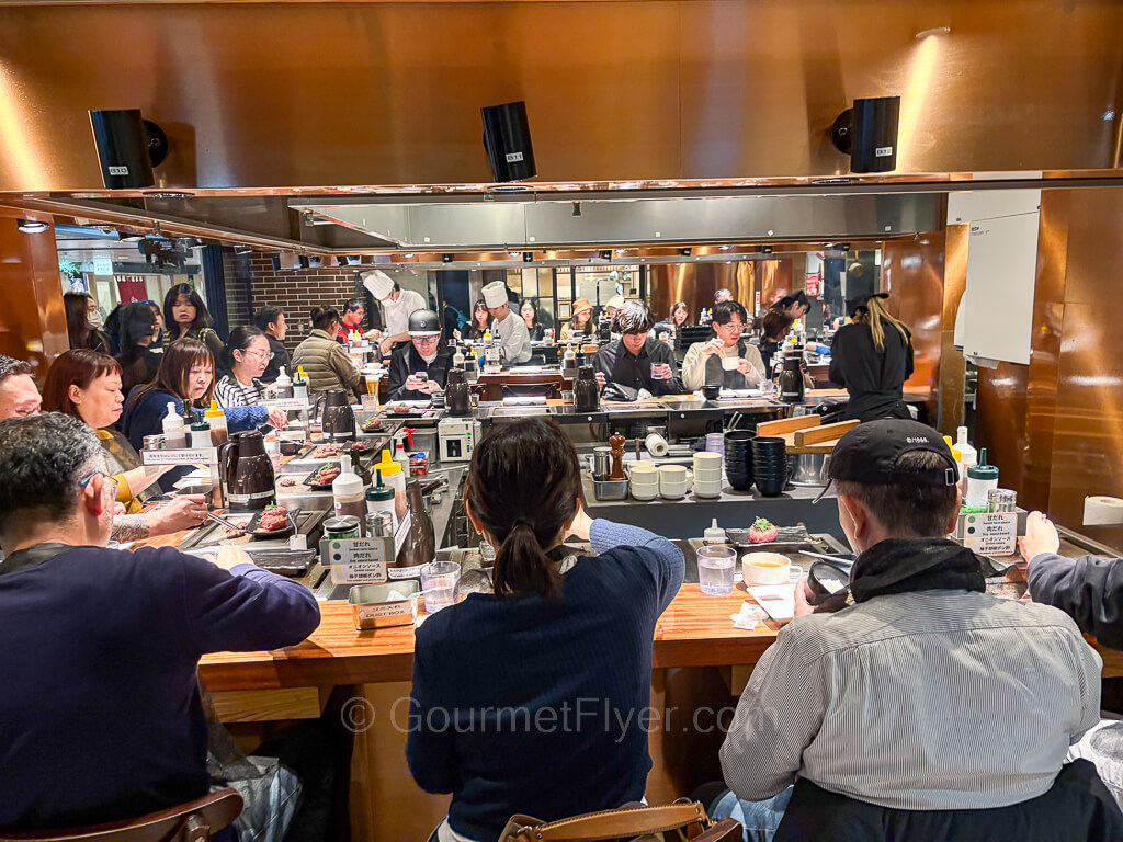 Diners sit around a U-shaped counter equipped with a teppan grill.