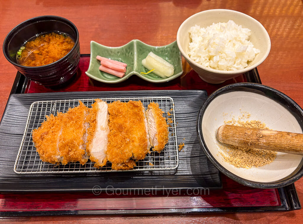 A dinner set on a meal tray includes fried pork cutlet, a bowl of white rice, and soup.