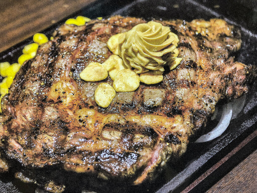 A large slab of grilled steak is served on an iron platter with a garnish of butter and garlic on top.
