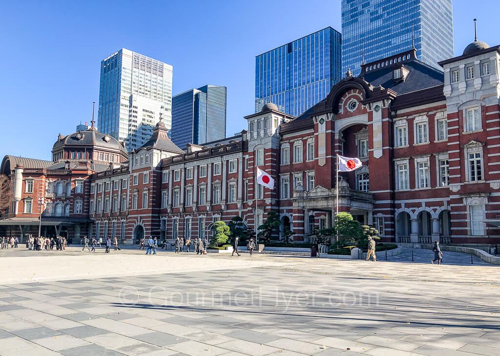 The iconic red brick building of the Marunouchi side of Tokyo Station, with two Japanese flags at the main entrance.