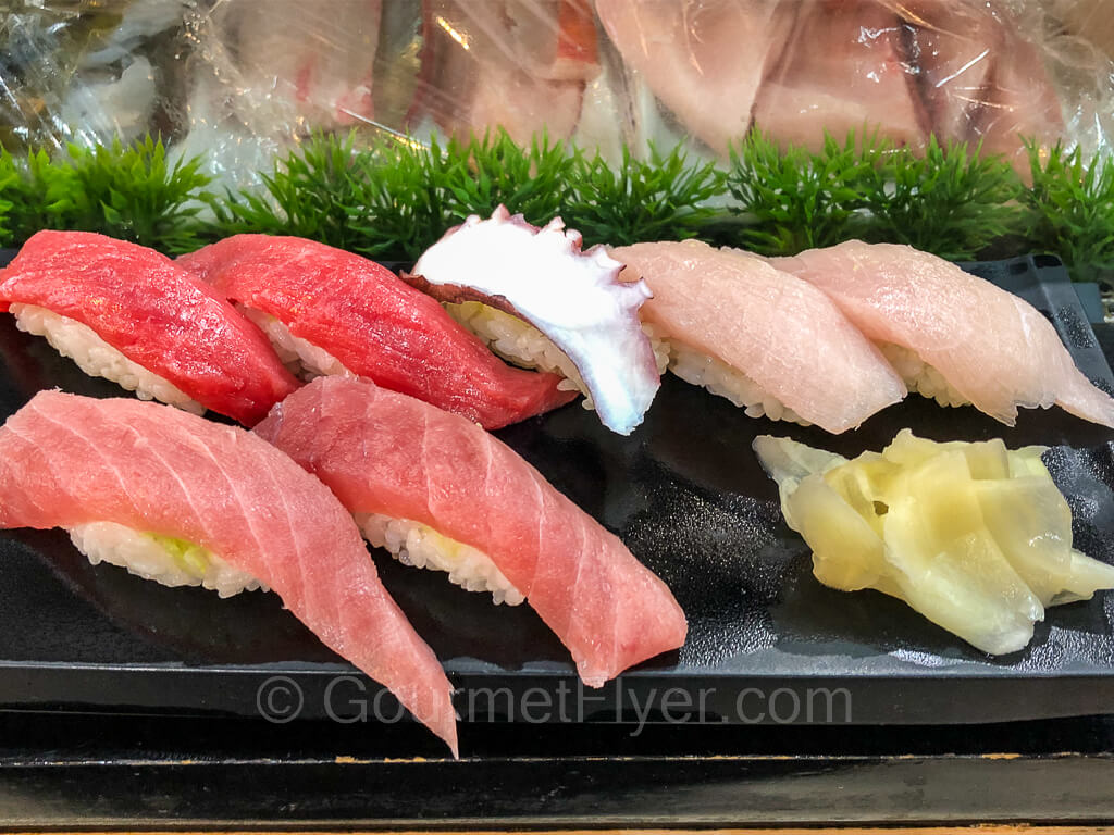 A platter of sushi includes red tuna, fatty tuna, octopus, yellow tail, and garnished with ginger slices.