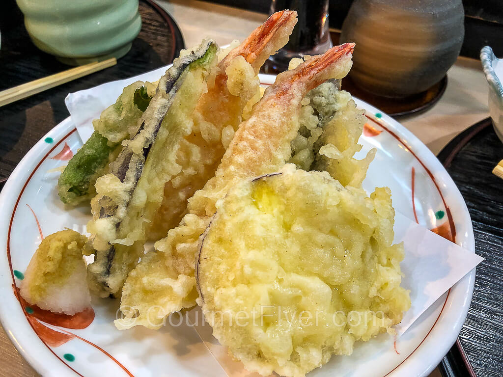 A plate of tempura with shrimps, fish, and vegetables.