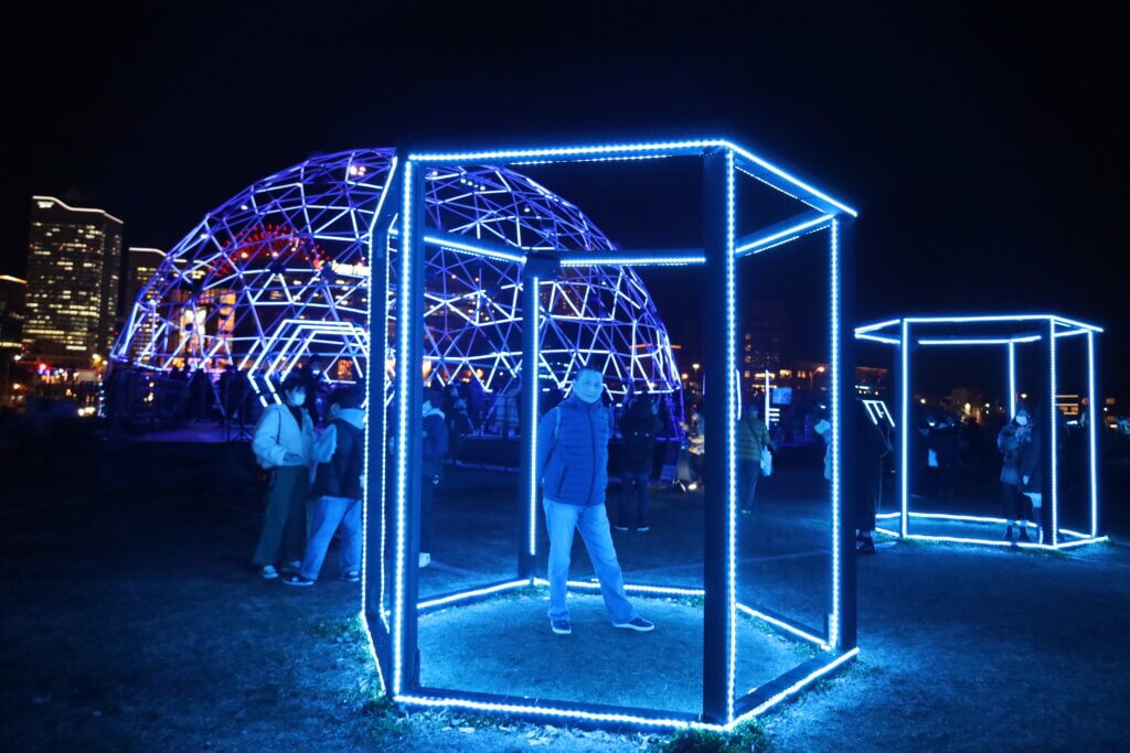 The Gourmet Flyer is posing inside a structure lit by neon tunes with the dome in the background.