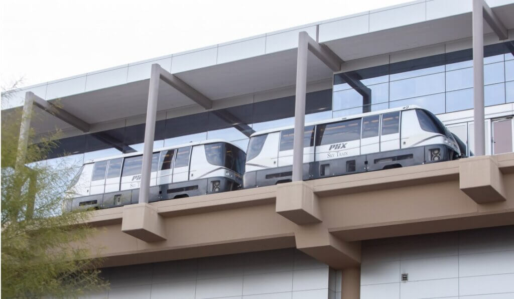 The PHX Sky Train with 2 cars is shown on an overpass approaching an airport terminal.