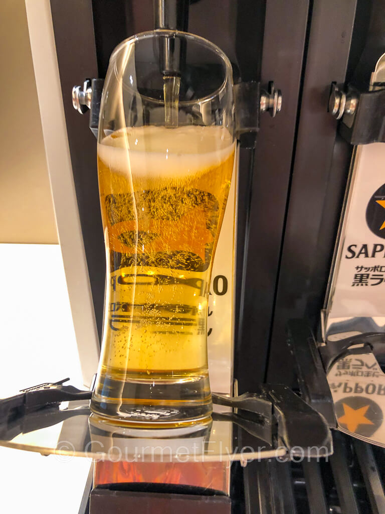 A beer glass is being filled by the automated beer machine and is almost full.