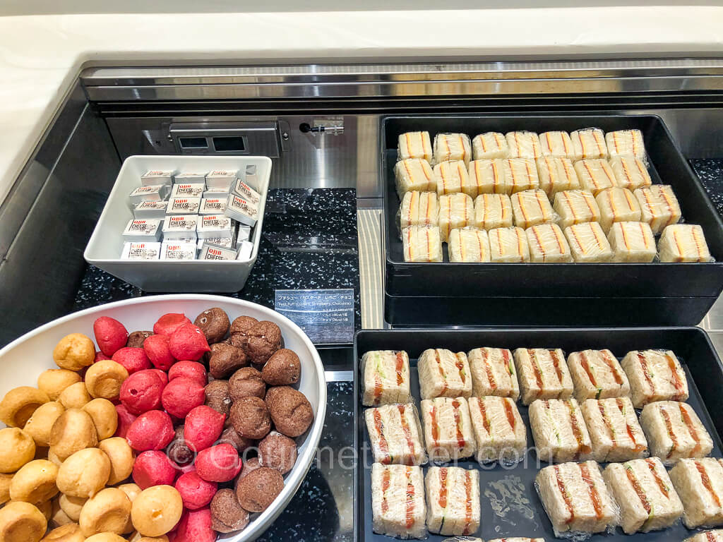 Two trays full of finger sandwiches are accompanied by a large bowl of mini cream puffs on the left.