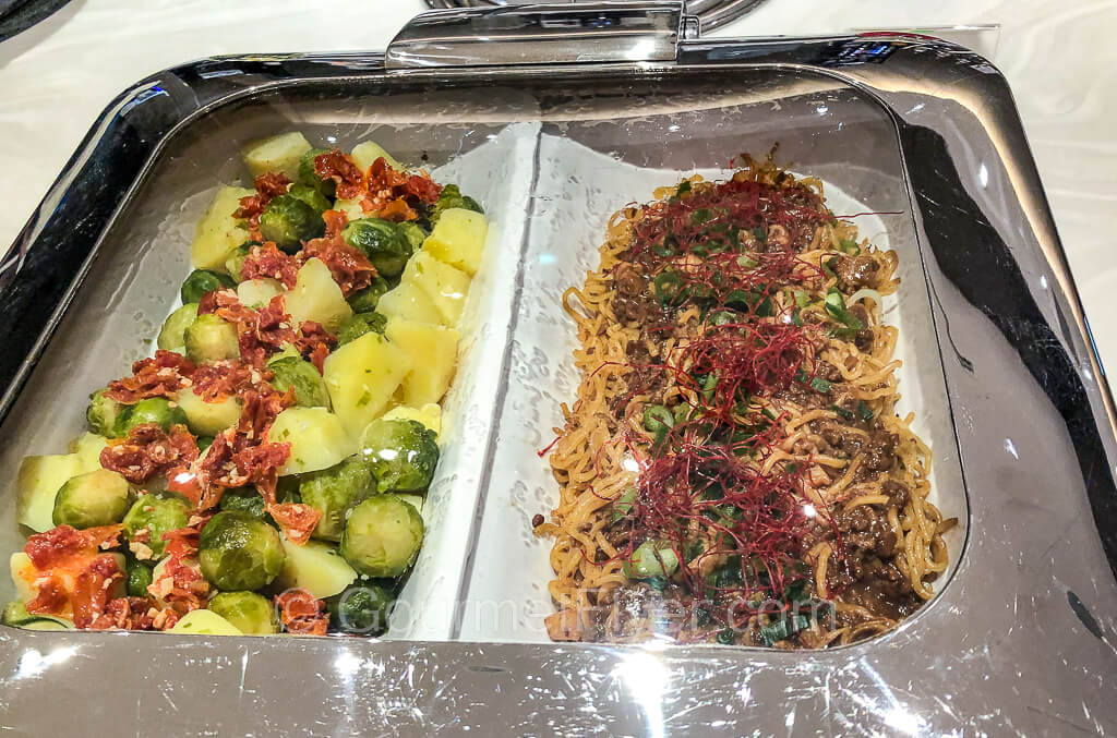 A tray with sauteed veggies such as Brussell sprouts and potatoes on the left and fried noodles on the right.