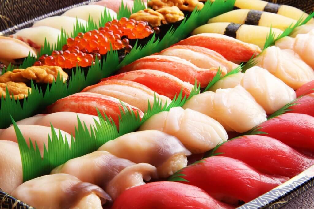 A large platter of sushi with a variety of fish such as red tuna in front and followed by white fish and crab meat.