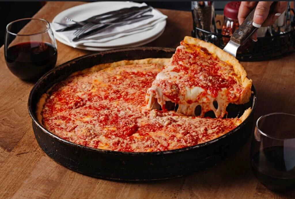 A slice of a deep-dish pizza is lifted from the pan by a spatula.