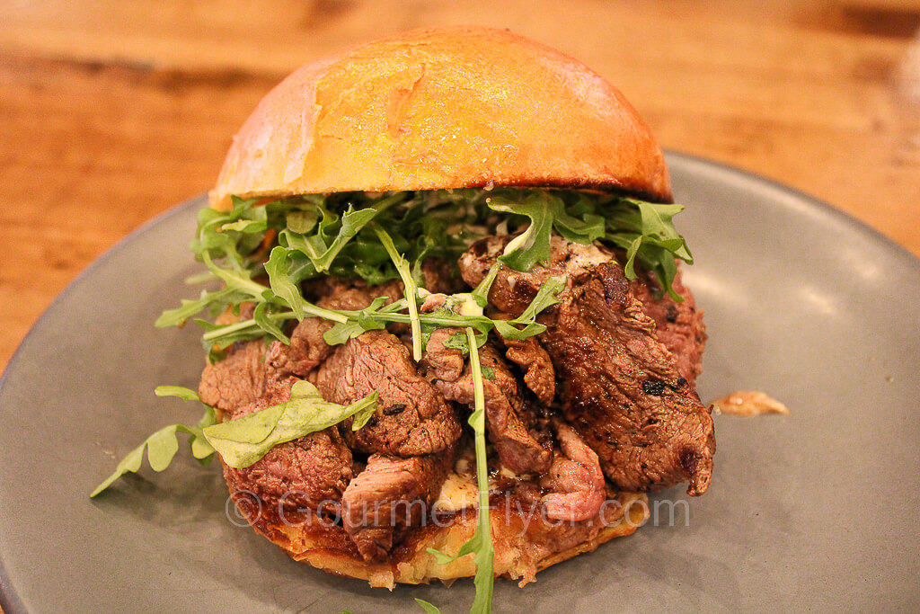 A stack of sliced steak topped with arugula is sandwiched in a bun.