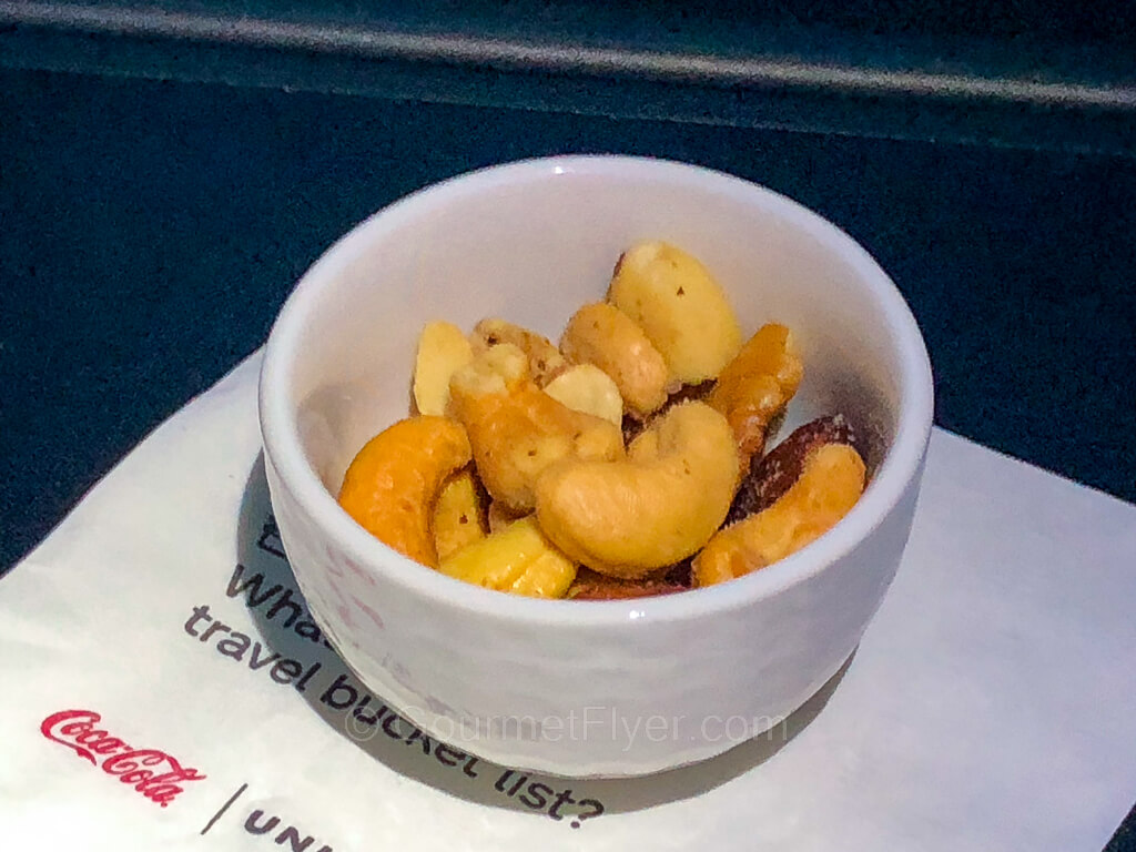 A small bowl of mixed nuts sits on a napkin on the tray table.