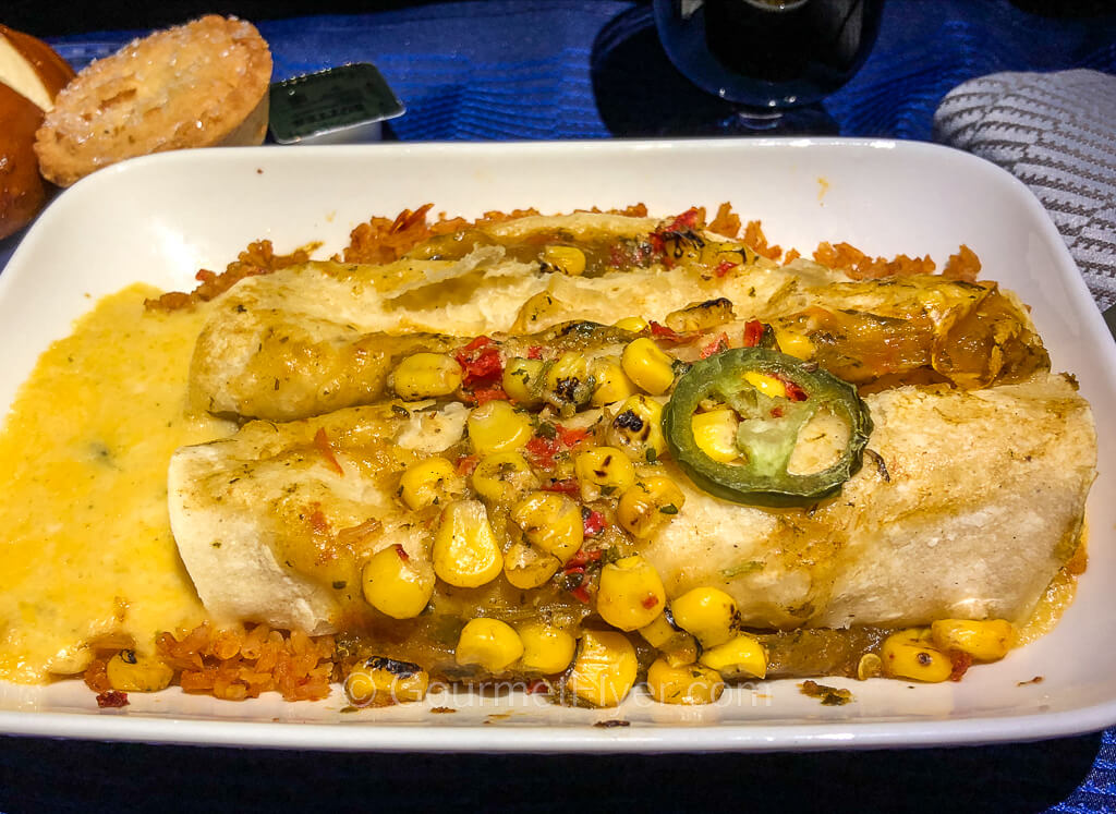 Two enchiladas are served with melted cheese on a bed of rice and topped with kernels of corn.